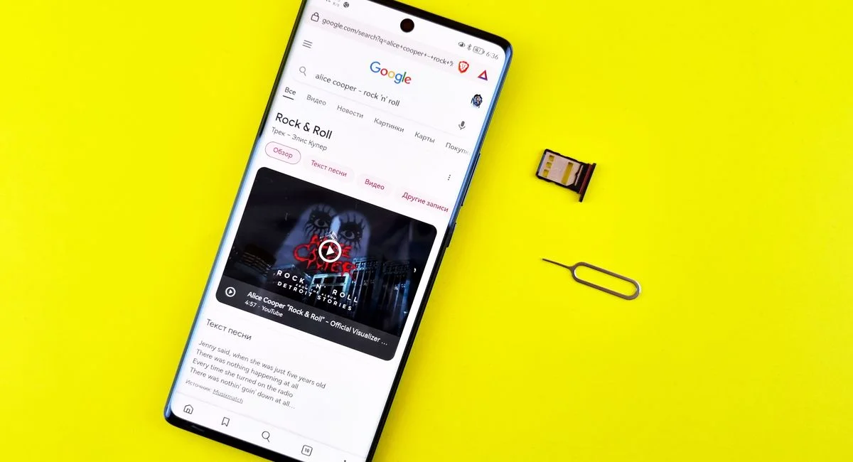 A smartphone with a Google search on a vibrant yellow surface, SIM card, and ejector pin visible.