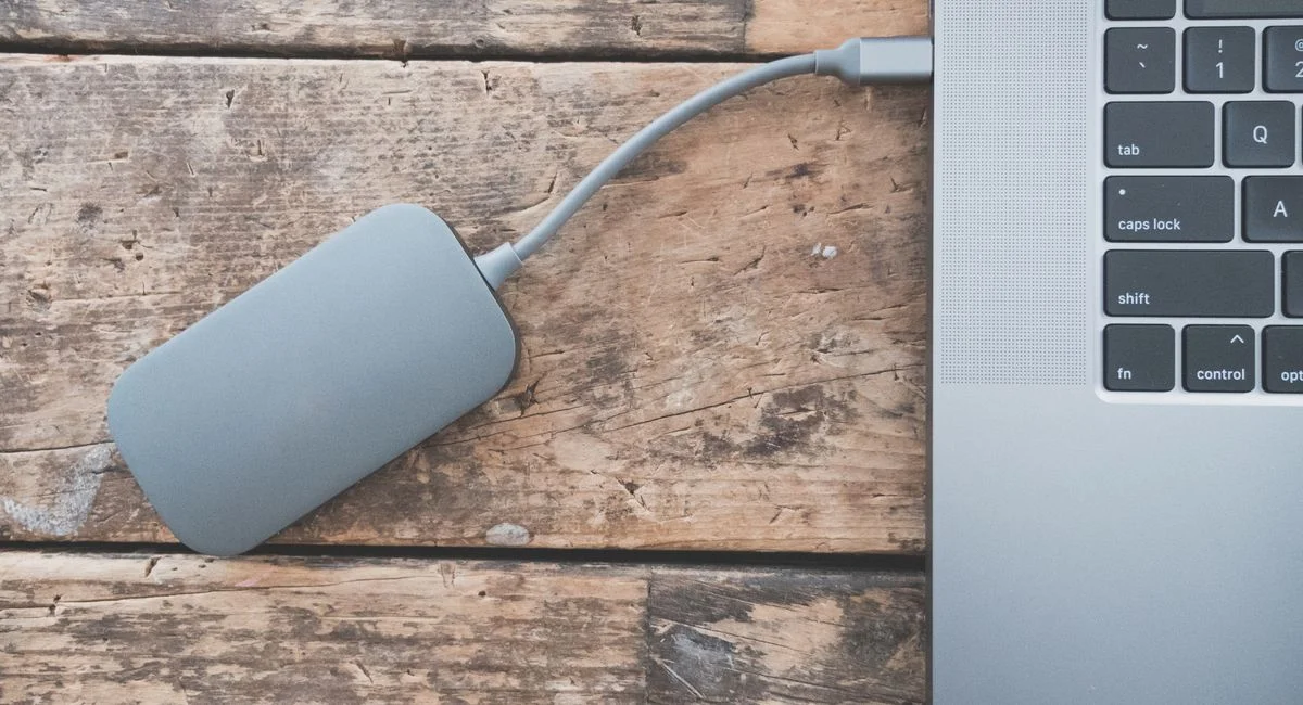 Close-up of an external hard drive connected to a laptop on a rustic wooden table.