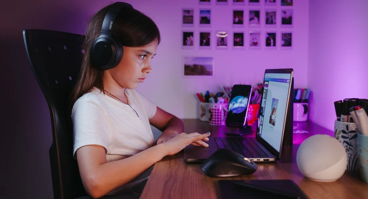 Girl with headphones using a laptop at her desk indoors, focused and engaged in a cozy atmosphere.