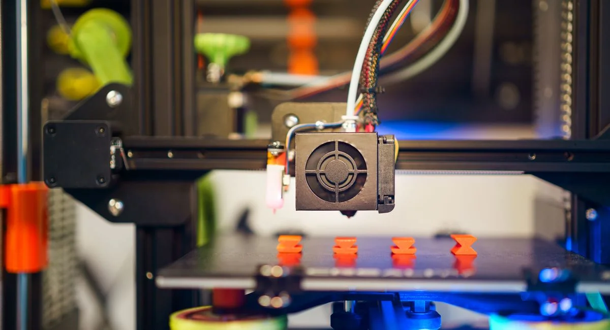 Detailed view of a 3D printer in action, fabricating small plastic pieces indoors.