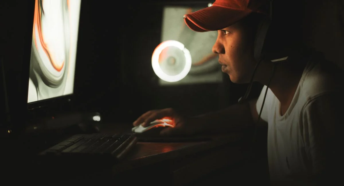 Young man gaming intensely in a dark room with neon lights, side view shot.