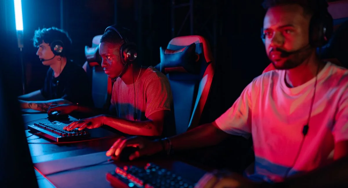 Three gamers immersed in a competitive setting with neon lighting, using keyboards and wearing headsets.