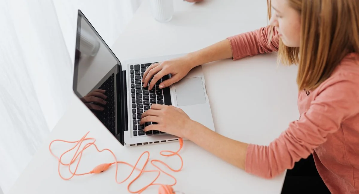 Teenage girl focused on laptop, wearing headphones, in a modern minimalistic setting.